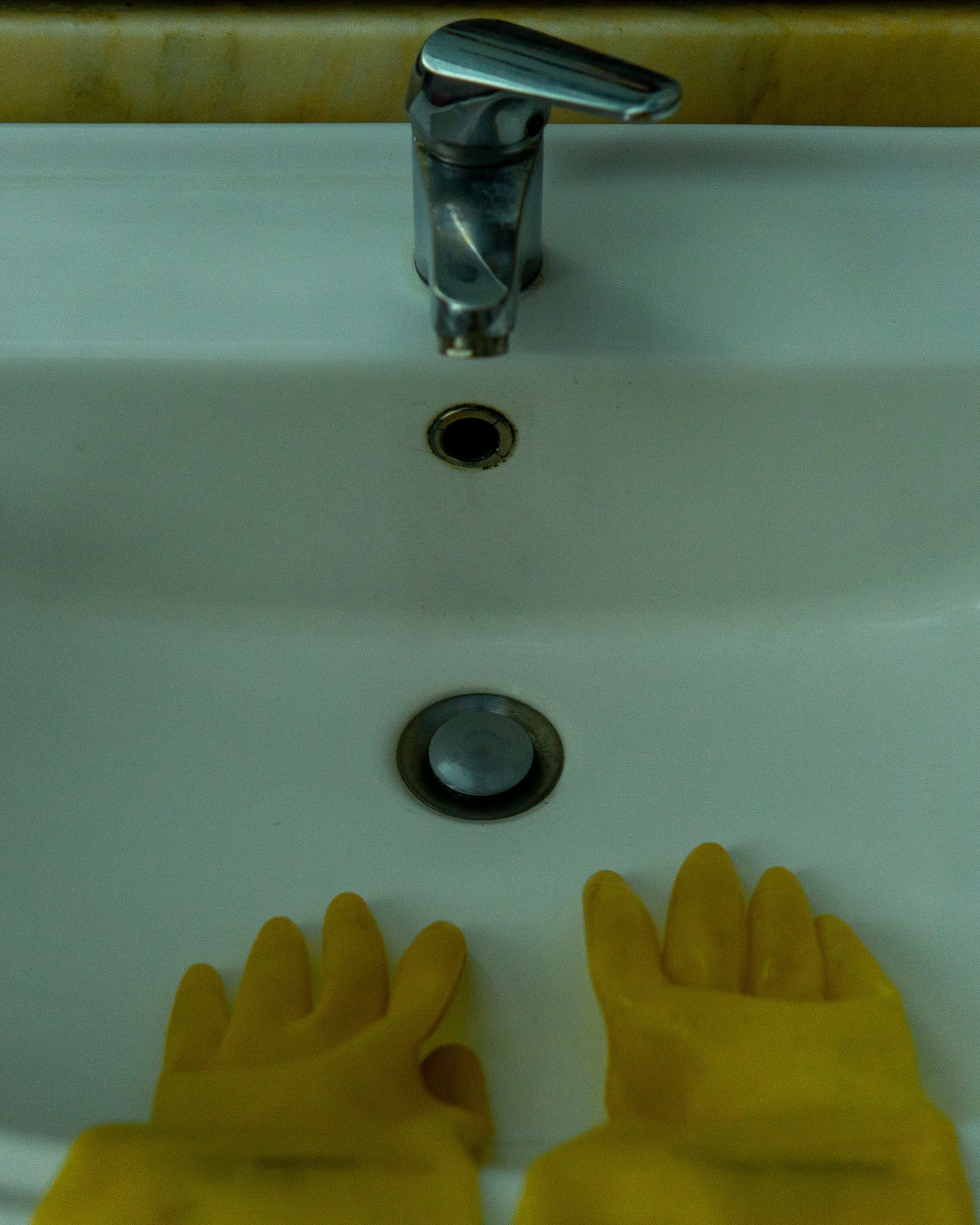 Gloved hand reaching toward a bathroom basin faucet